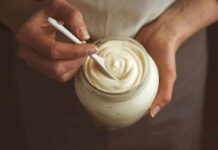 Hands holding a jar of creamy yogurt with a spoon