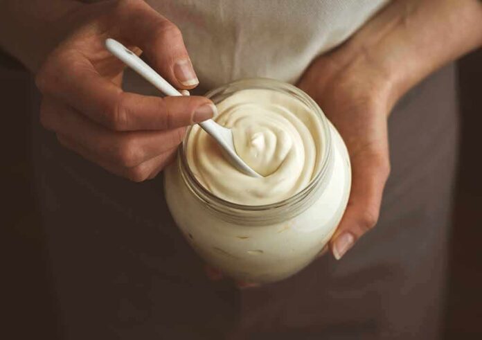 Hands holding a jar of creamy yogurt with a spoon