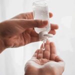 Hands dispensing sanitizer gel from a small bottle