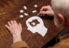 Hands assembling a head-shaped jigsaw puzzle on a wooden table