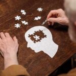Hands assembling a head-shaped jigsaw puzzle on a wooden table