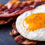 Fried egg with crispy bacon on dark surface