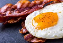 Fried egg with crispy bacon on dark surface
