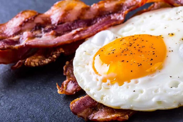 Fried egg with crispy bacon on dark surface