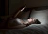 Woman lying in bed looking at smartphone