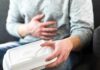 Person holding stomach with takeout container on lap