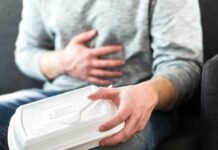 Person holding stomach with takeout container on lap