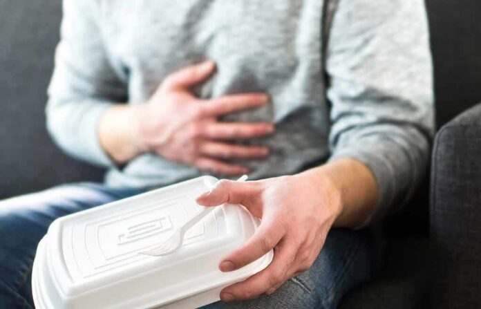 Person holding stomach with takeout container on lap