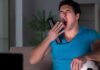 Man yawning on couch holding TV remote and soccer ball