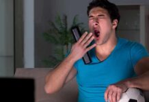 Man yawning on couch holding TV remote and soccer ball