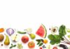 Assorted fresh fruits and vegetables arranged along the bottom on white