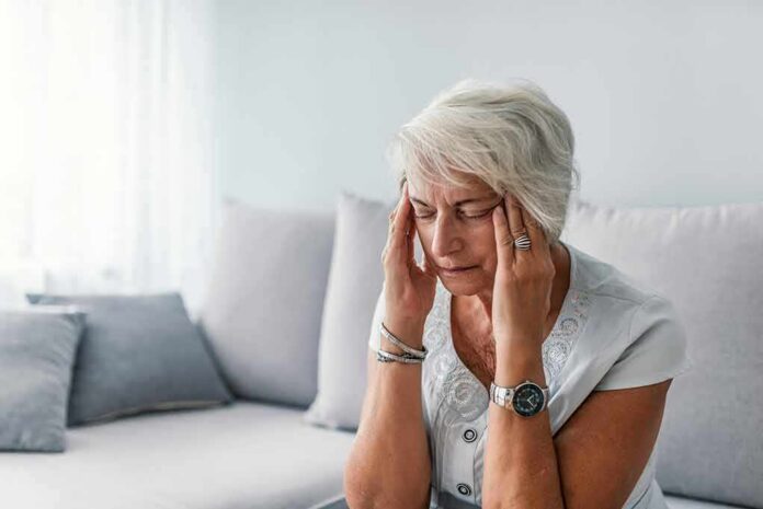 Older woman sitting on a couch holding her temples