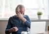 Older man rubbing his eye while sitting at a laptop