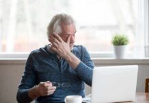 Older man rubbing his eye while sitting at a laptop