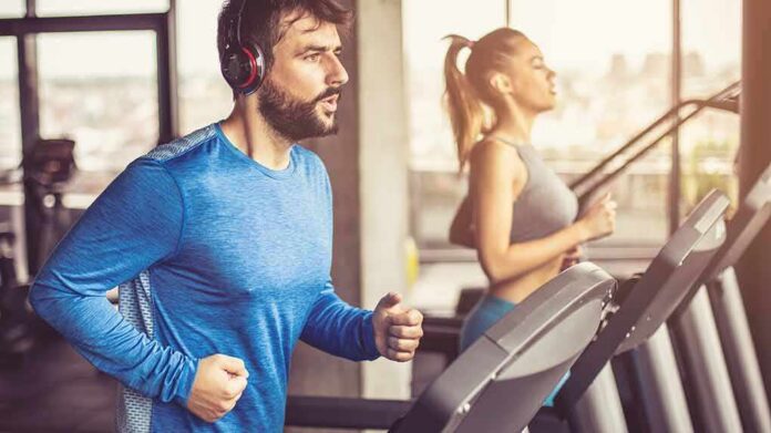 Man in blue long-sleeve running on a treadmill with headphones