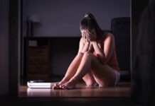 Woman sitting on floor covering face beside a bathroom scale