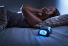 Person lying awake in bed beside a glowing digital alarm clock