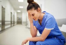 Nurse in blue scrubs sitting with head in hand