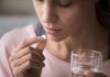 Woman holding a white pill and a glass of water