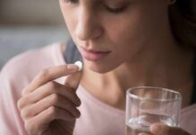 Woman holding a white pill and a glass of water