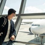 Traveler wearing a mask looks at airplane through airport window