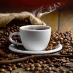 steaming cup of coffee among roasted beans