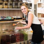 Shop worker scooping dried fruit into a bag at bulk bins