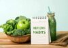 Basket of green vegetables with apple, notebook, and green smoothie