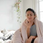 Constant Throat Clearing? Why It’s Not Random Woman wrapped in blanket touching her throat