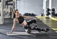 Woman foam rolling thigh on yoga mat in gym