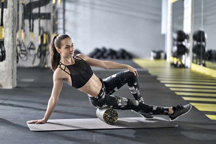 Woman foam rolling thigh on yoga mat in gym