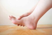 Walk Hack Cuts Arthritis Pain Fast Hand holding the arch of a bare foot on a wooden floor