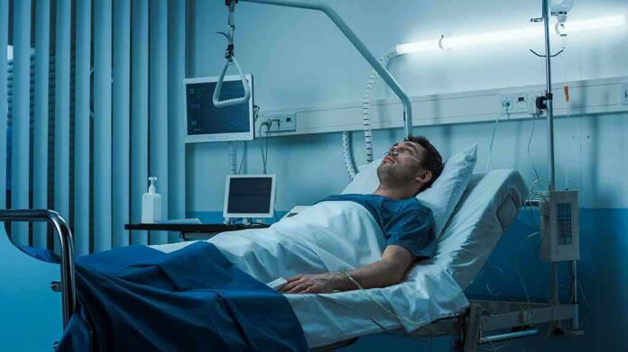 shutterstock_1190998111 Man lying in a hospital bed with monitors and IV equipment