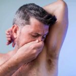 Man covering his nose while smelling his armpit