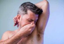 Man covering his nose while smelling his armpit