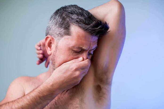 Man covering his nose while smelling his armpit