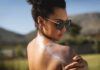 Woman in sunglasses applying sunscreen to her shoulder outdoors