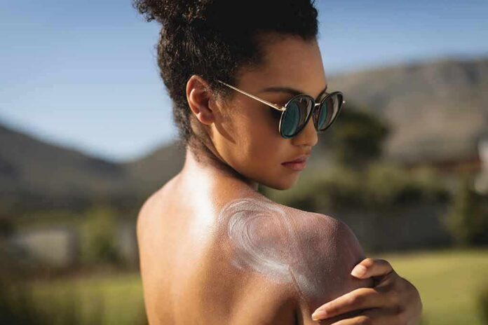 Woman in sunglasses applying sunscreen to her shoulder outdoors