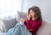 Medicine’s Blindspot: Why is it so hard to cure the common cold? Woman on couch with tissue and mug