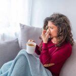 Medicine’s Blindspot: Why is it so hard to cure the common cold? Woman on couch with tissue and mug