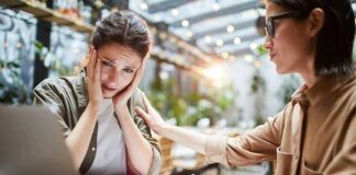 Two women at a table, one comforting the other