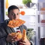 Night Cravings Explained – Why 8 P.M. Appetite Spikes man in robe eating pizza at open refrigerator