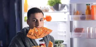 man in robe eating pizza at open refrigerator