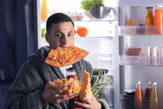 shutterstock_1447848791 man in robe eating pizza at open refrigerator