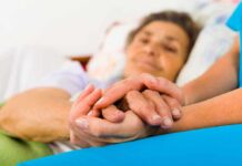 Caregiver holding hands with an elderly patient in bed