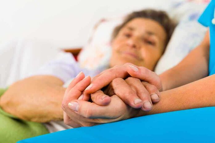 shutterstock_161459273-1 Caregiver holding hands with an elderly patient in bed