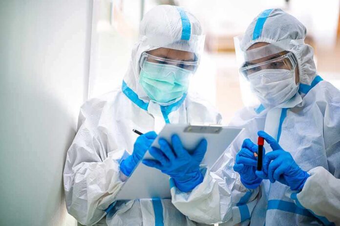 Two healthcare workers in full PPE reviewing a clipboard