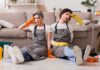Two tired cleaners sitting on the floor by a sofa