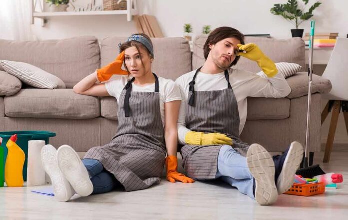 shutterstock_1696378792 Two tired cleaners sitting on the floor by a sofa