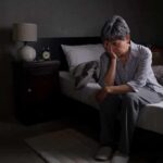 3 A.M. Wake-Ups: Normal Aging – Or Big Red Flag? Older adult sitting on bed with head in hand